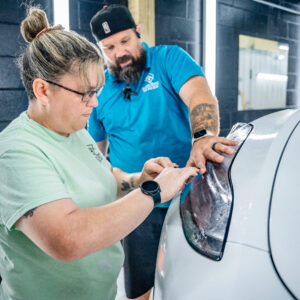 Brian and Amber from Summer Breeze Ceramic Coating & Mobile Detailing Inspecting Paint Protection Film (PPF) of a White Tesla