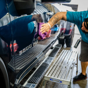 Brian, owner of Summer Breeze Ceramic Coating & Mobile Detailing, has just finished an exterior car detailing job on a truck and is polishing it with a purple towel, ensuring a spotless shine.