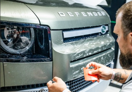 Brian, owner of Summer Breeze Ceramic Coating & Mobile Detailing, carefully applies car paint protection film to the front of a Land Rover.